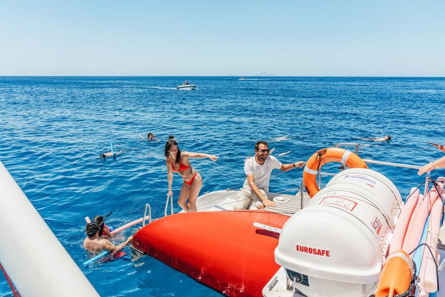 Santorini: Catamaran Tour with BBQ Dinner, Drinks, and Music - Red Beach from the water